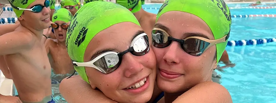 Due ragazze in cuffia ed occhialini si abbracciono in piscina