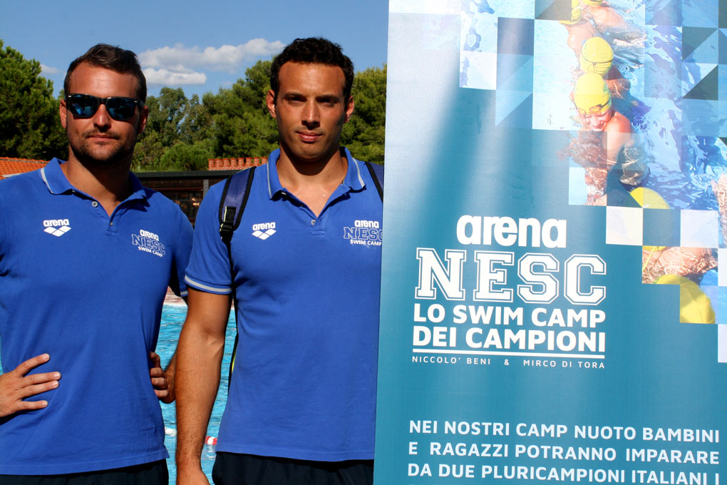 Niccolò Beni e Mirco Di Tora in posa davanti alla pubblicità dei camp nuoto NESC
